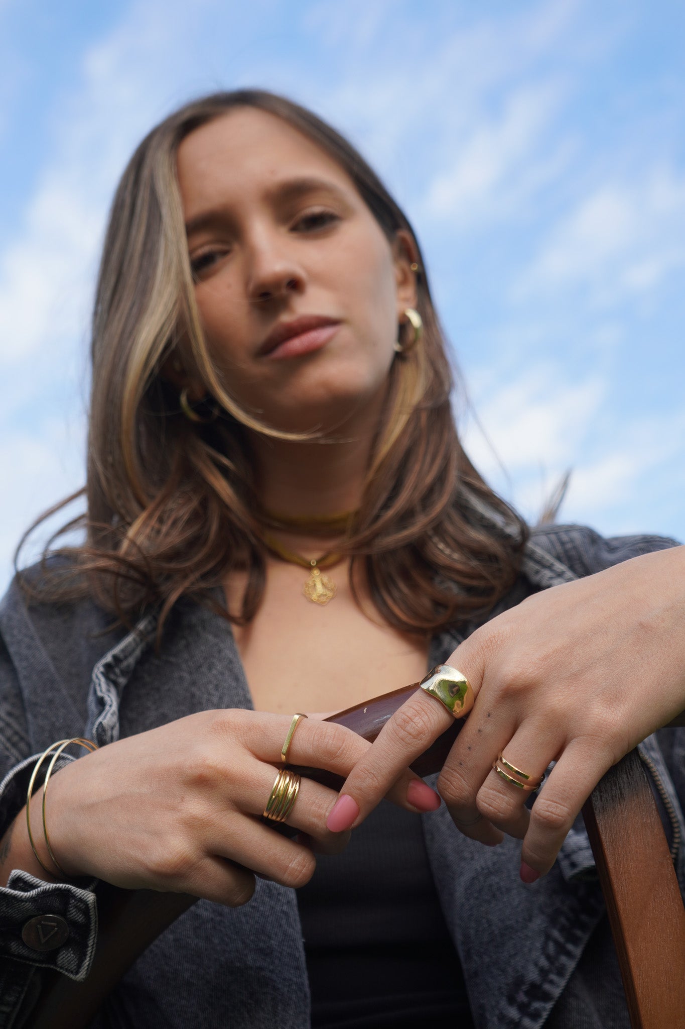 Mujer con anillos dorados, aros y collar con dije dorado, colección primavera de Maca Barros Joyas