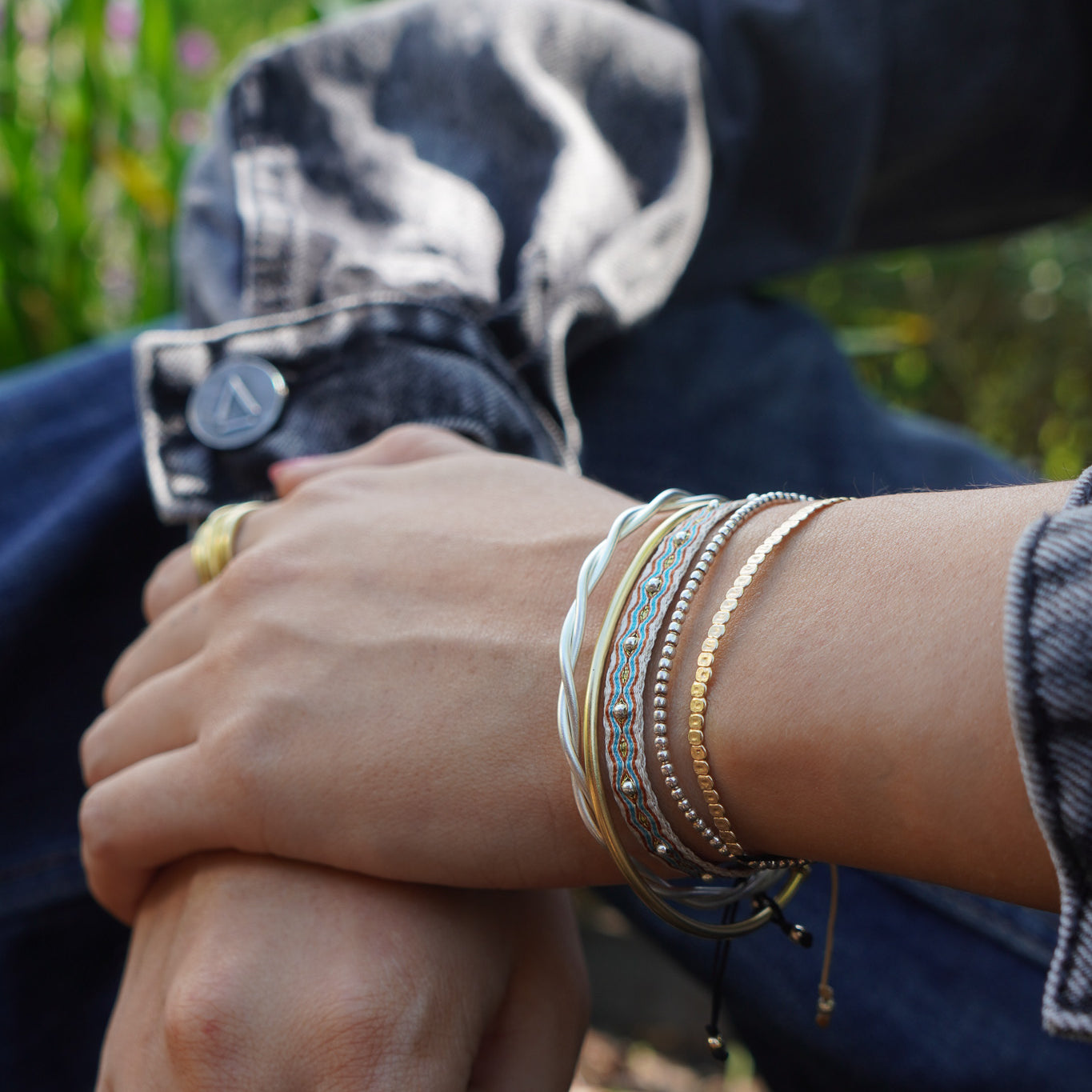 Pulseras tejidas a mano con cuentas plateadas y doradas junto a anillos dorados de Maca Barros Joyas