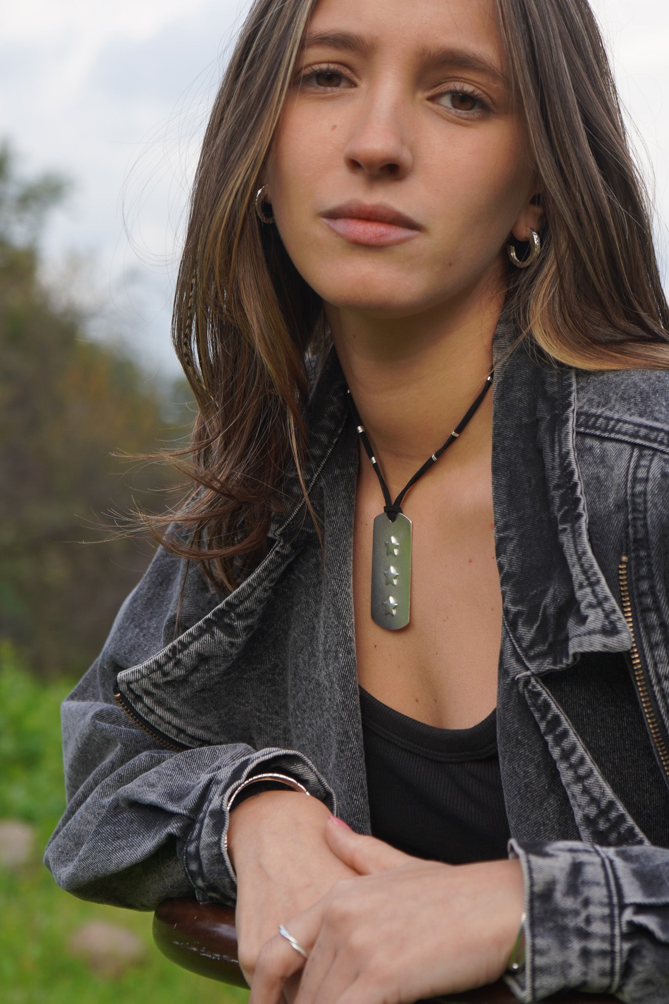 Mujer con collar de piedra verde en cordón negro, aros argolla y anillo plateado de Maca Barros Joyas