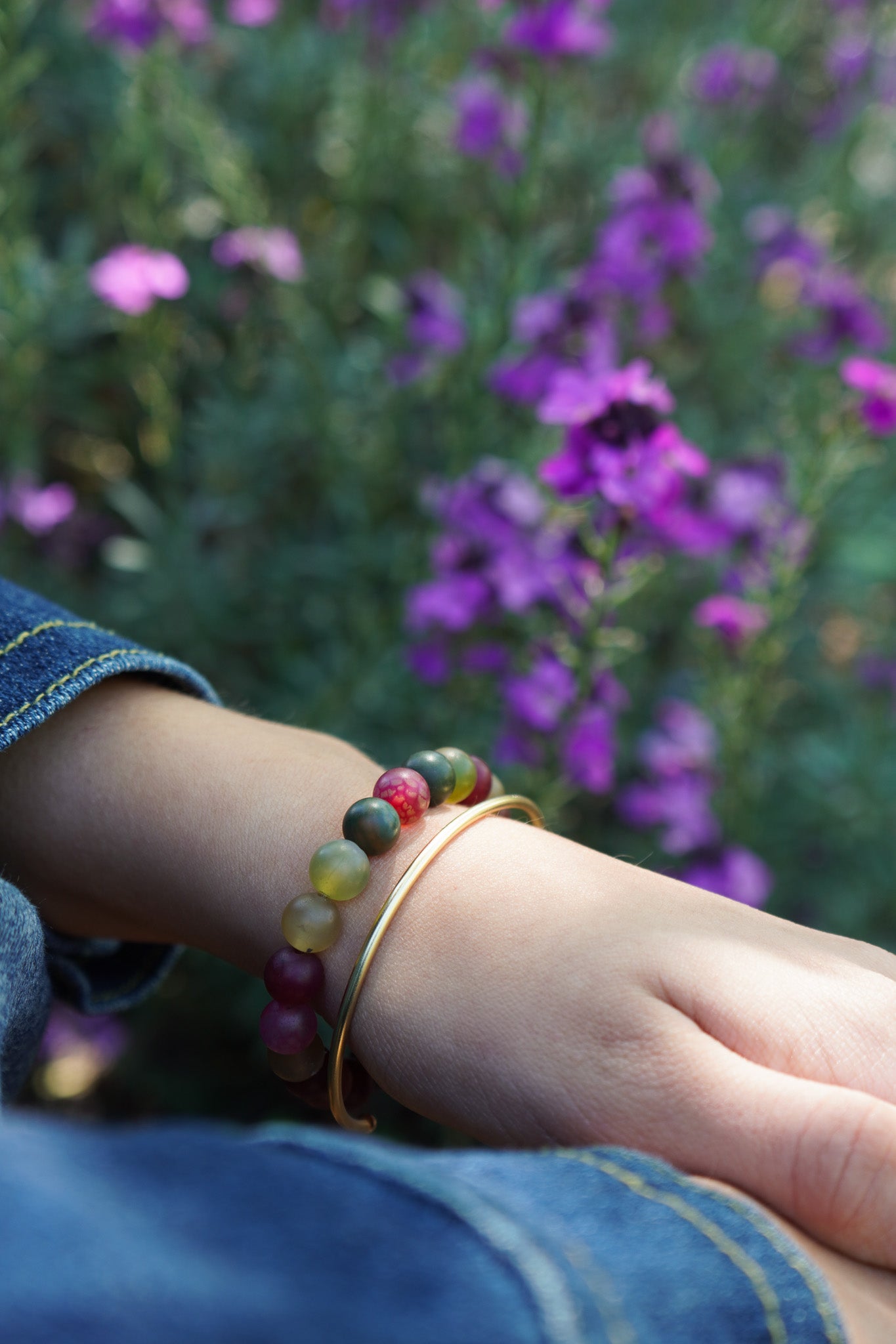 Pulsera de piedras naturales multicolor y brazalete dorado en muñeca, colección primavera de Maca Barros Joyas